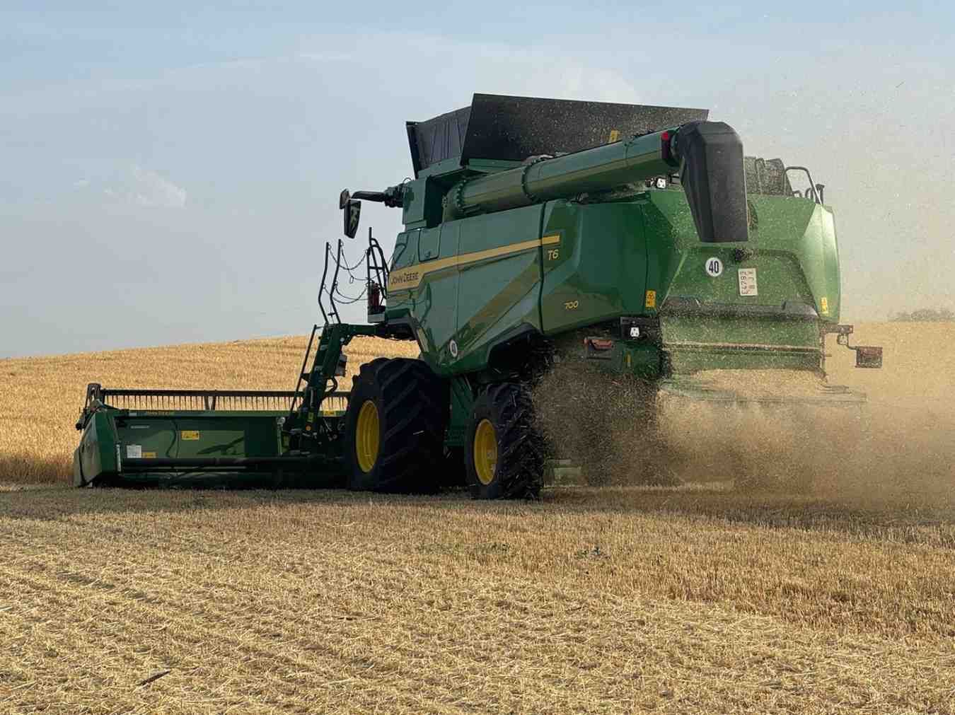 Una excavadora amarilla abre una zanja en un campo rocoso bajo un cielo despejado.