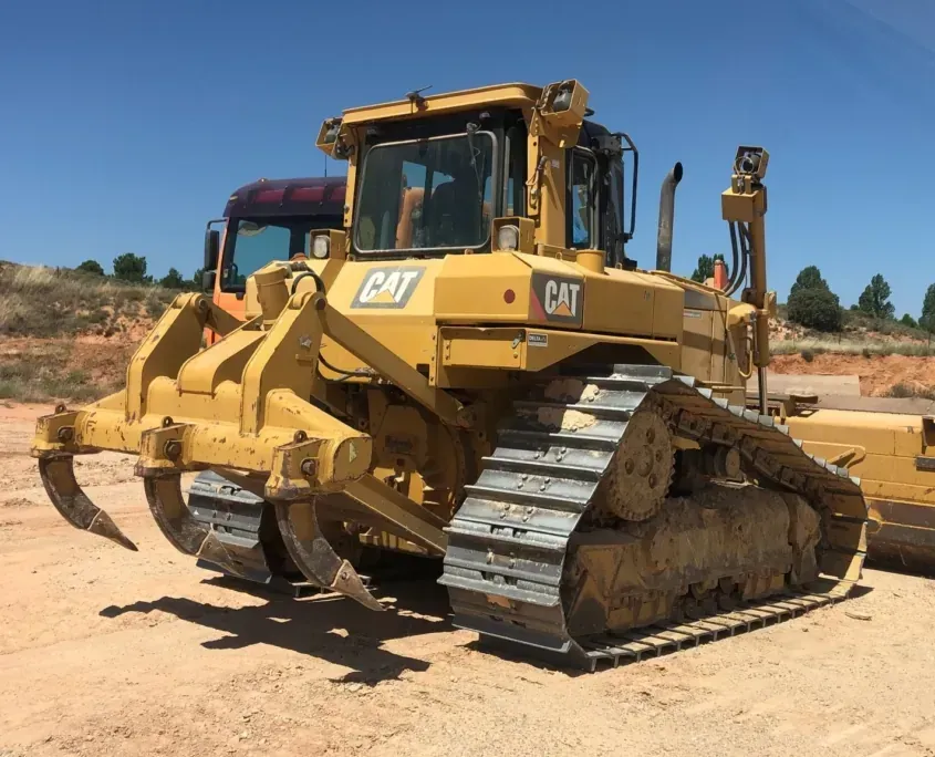 Bulldozer CAT amarillo en un terreno baldío bajo un cielo despejado, con la pala frontal levantada y las orugas visibles.