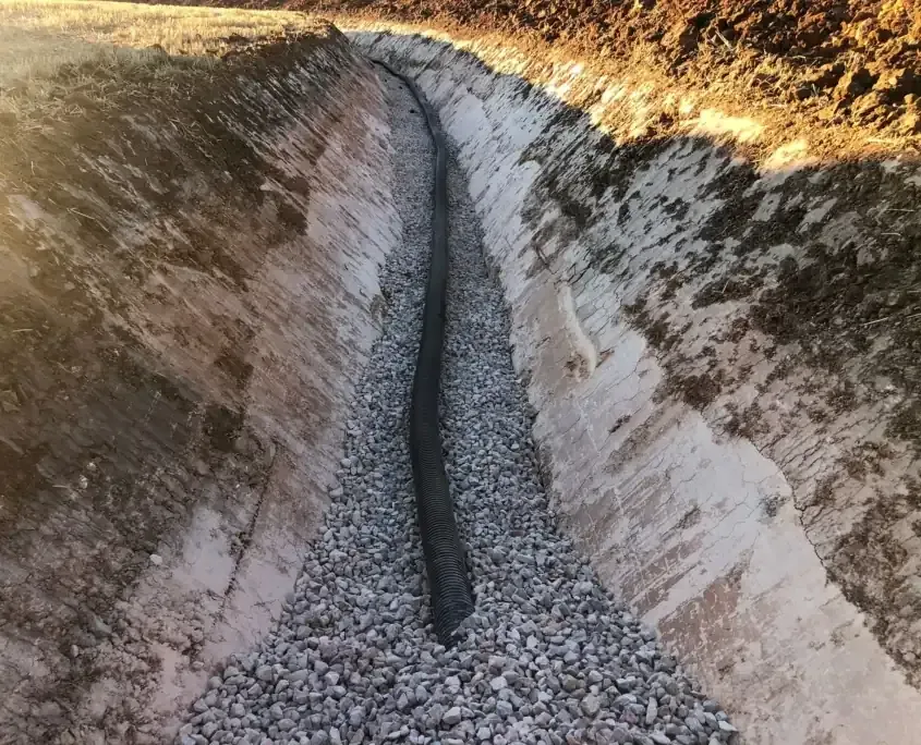 Una zanja de drenaje de hormigón revestida de grava y con una tubería negra que la recorre por el centro.