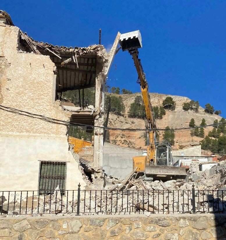 Obreros de la construcción y una excavadora junto a un camión volquete naranja en una zanja de tierra.