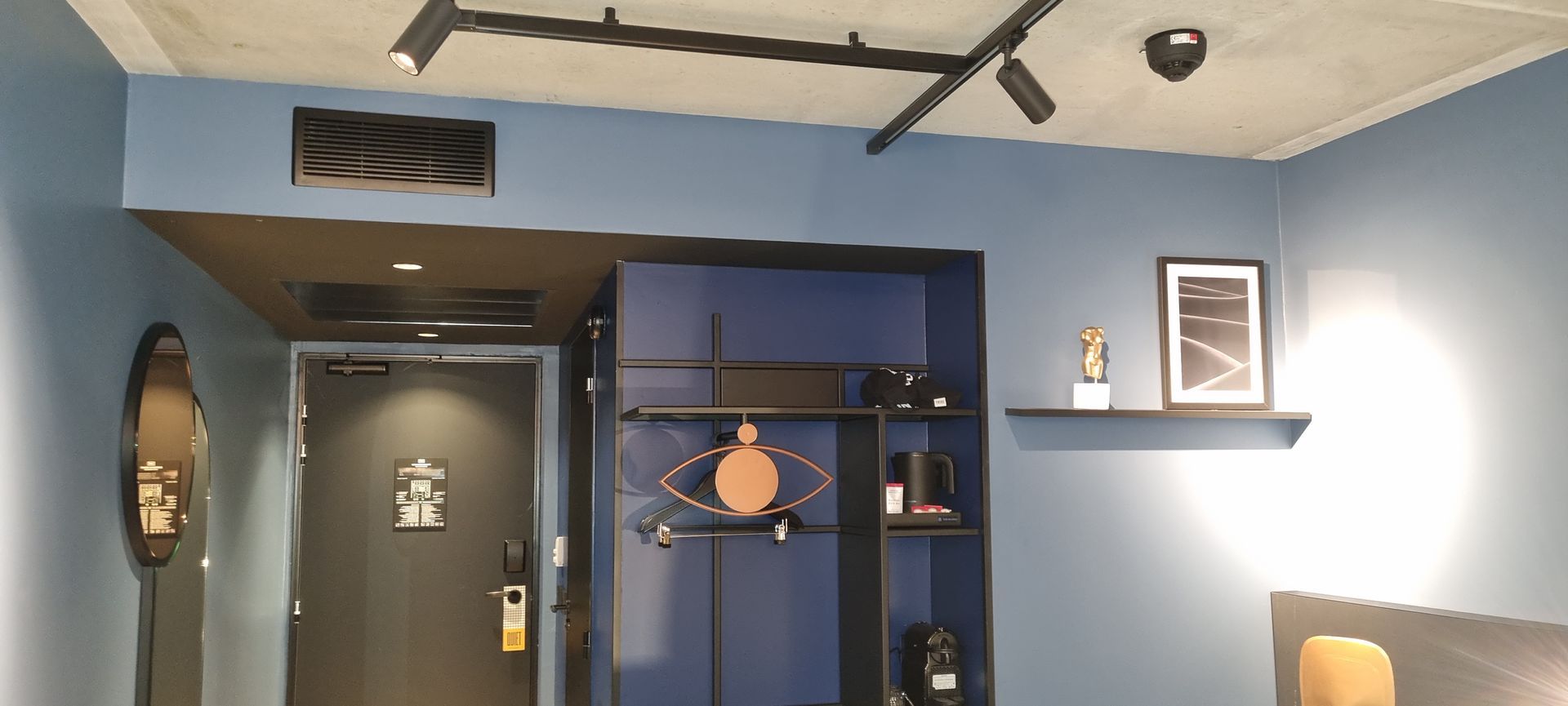 Une chambre d'hôtel moderne avec des murs bleus, une entrée sombre et des éléments décoratifs aux murs et au plafond.