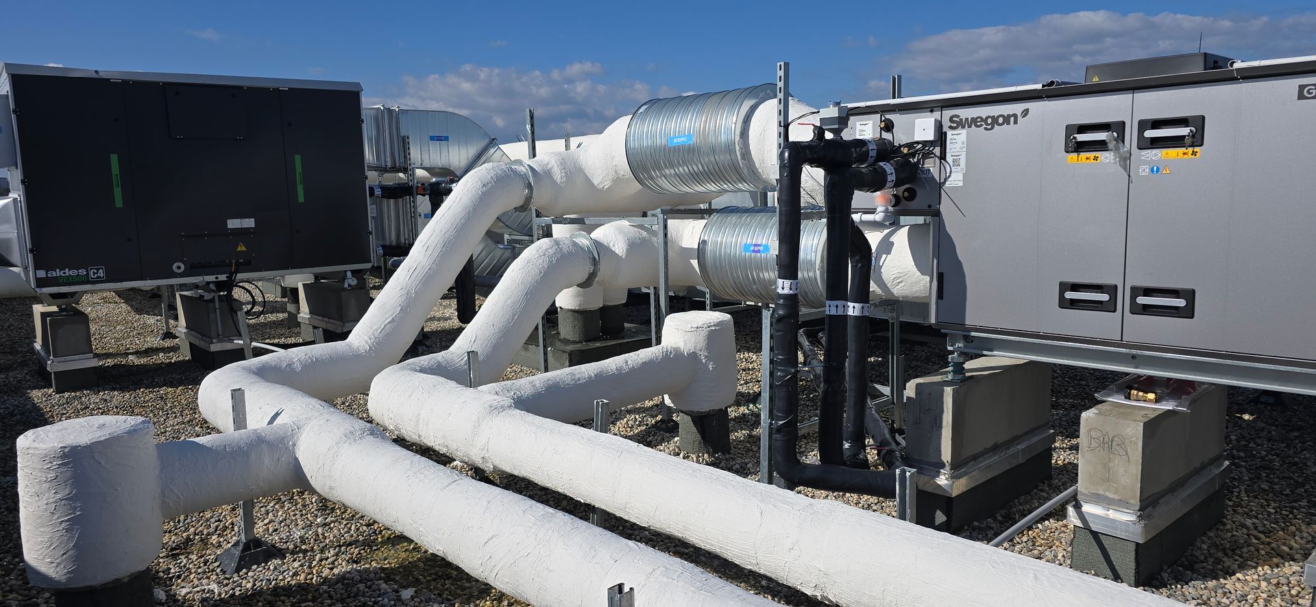 Équipement de climatisation sur le toit, avec des tuyaux isolés et un ciel bleu dégagé.