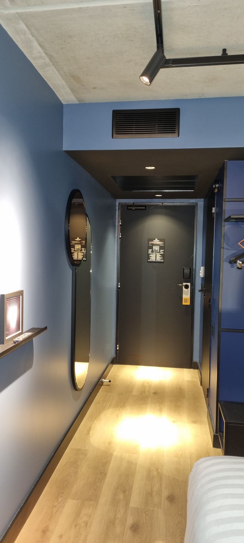 Couloir étroit d'hôtel aux murs bleus, au parquet et à la porte noire. Un long miroir est accroché au mur de gauche.