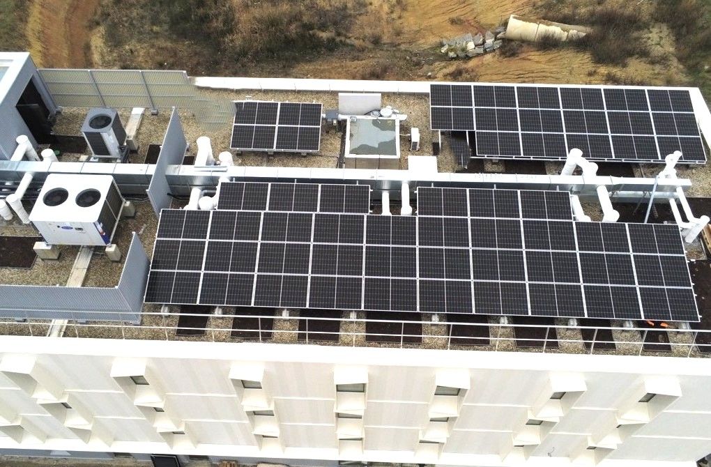 Vue aérienne du toit d'un bâtiment avec des panneaux solaires installés, des unités de climatisation et de chauffage.