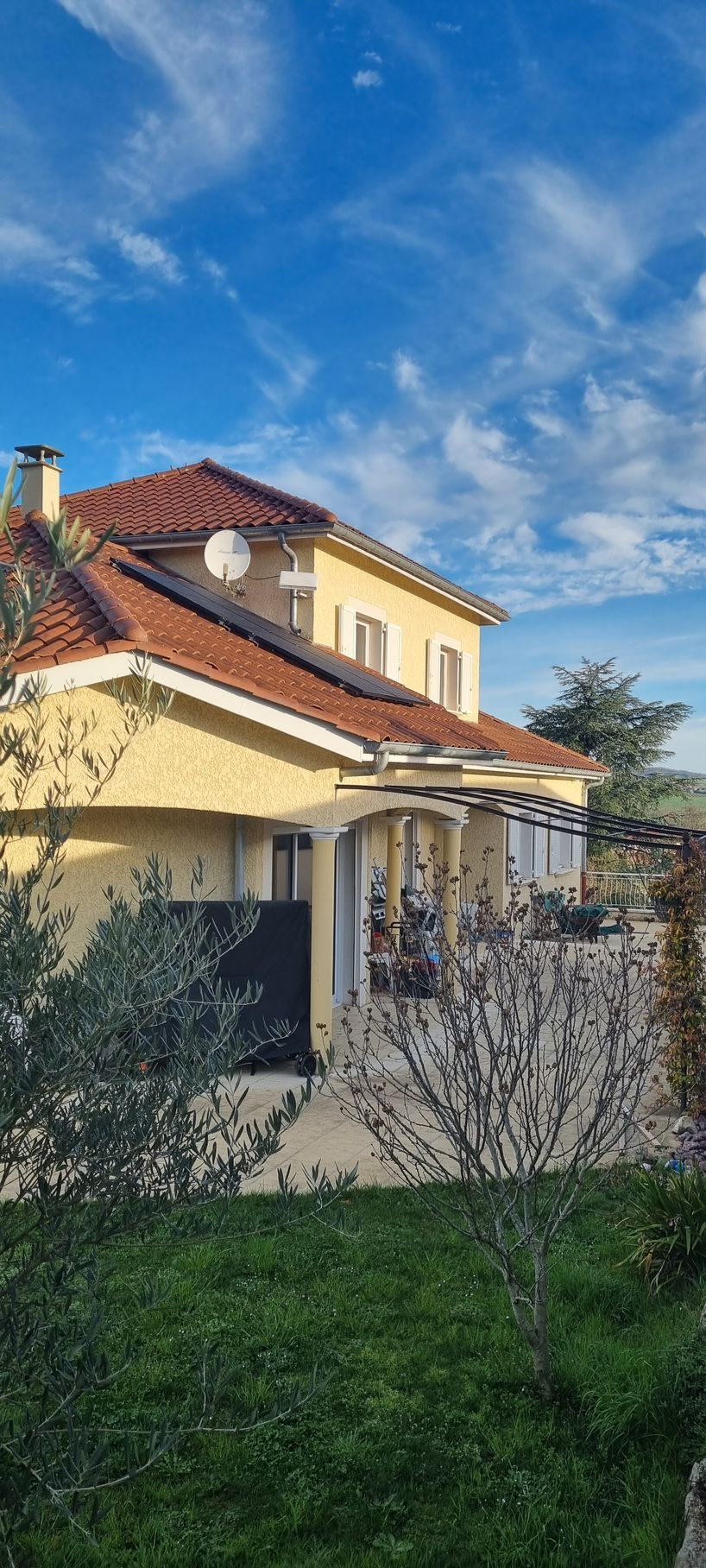 Maison jaune au toit rouge et ciel bleu. Végétation au premier plan.