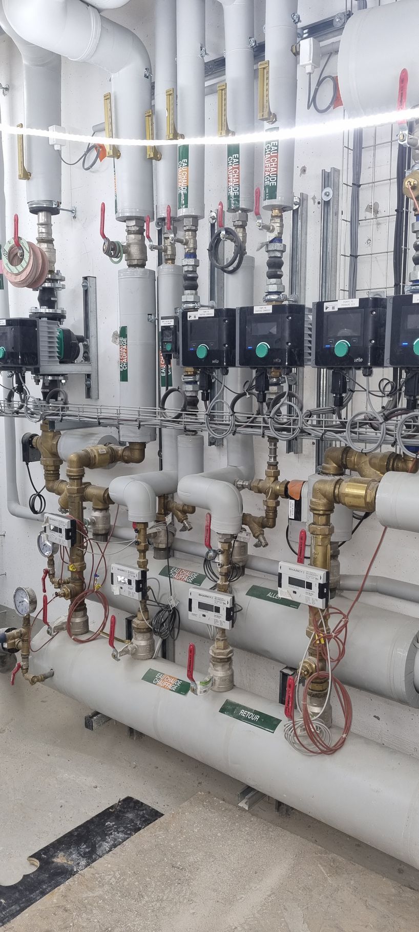 Système complexe de tuyauterie industrielle avec vannes, manomètres et composants électriques, en intérieur.