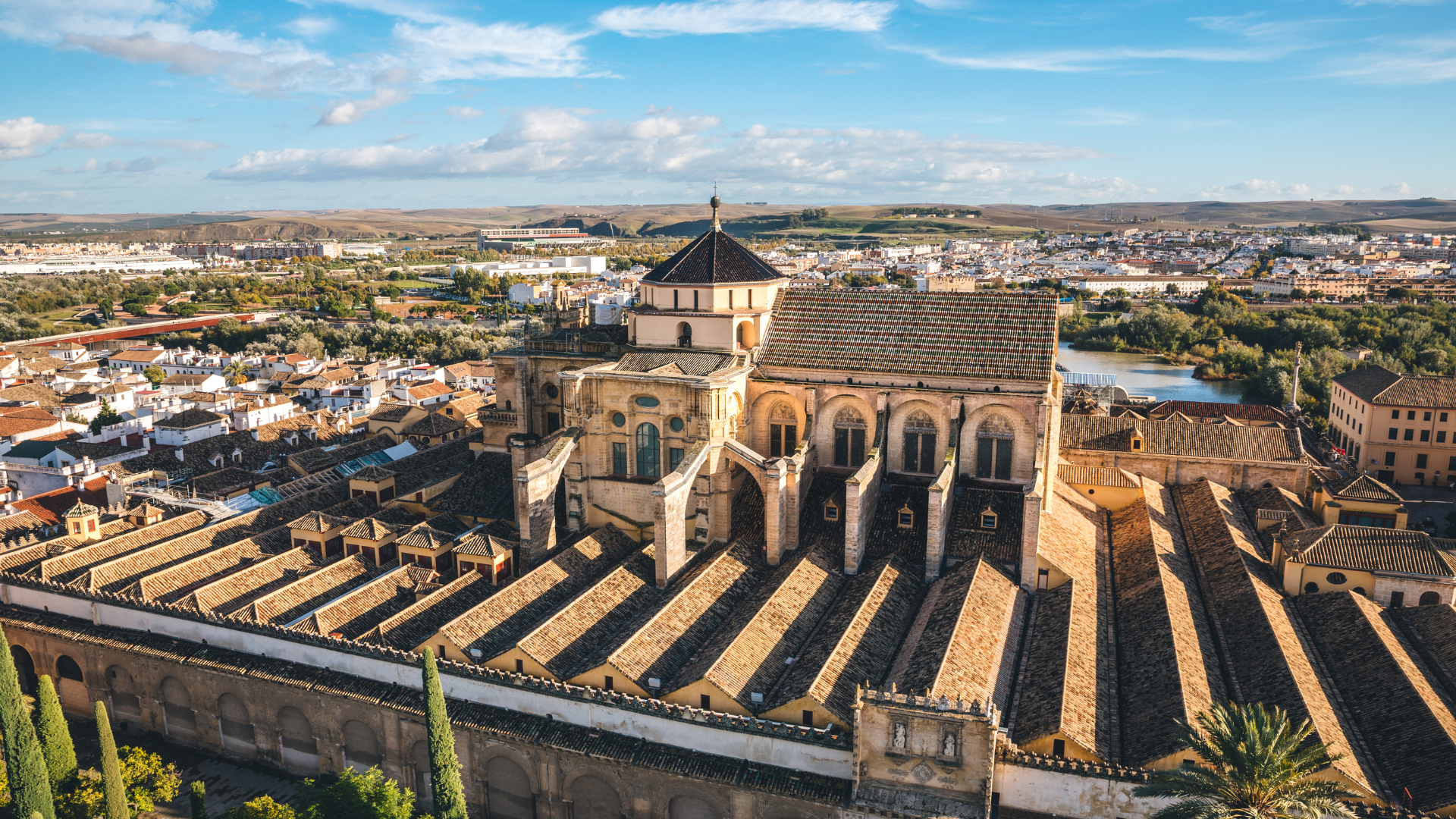 Vista aérea de la Mezquita-Catedral de Córdoba, España, con la ciudad y el río circundante visibles bajo un cielo azul.