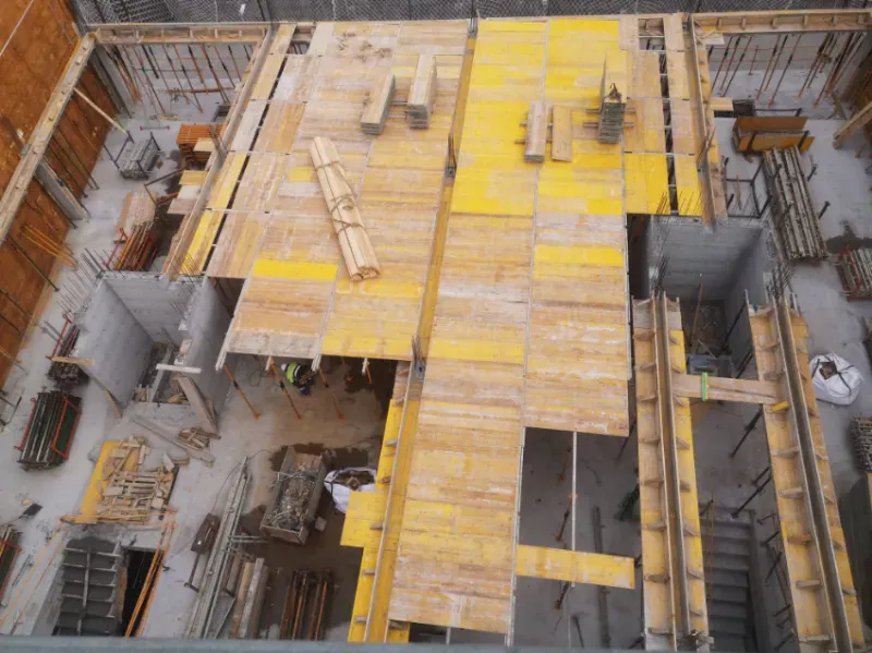 Obra en construcción con encofrado de madera contrachapada amarilla y andamios en el foso de los cimientos de un edificio.