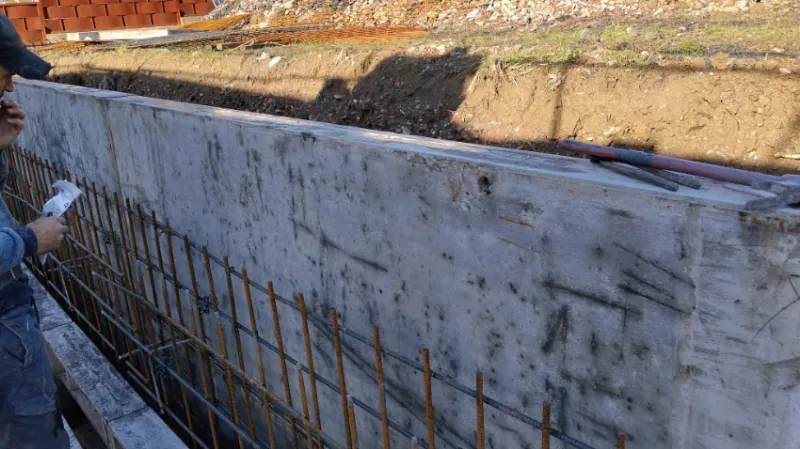 Obrero inspeccionando barras de refuerzo y muro de hormigón en una obra de construcción.