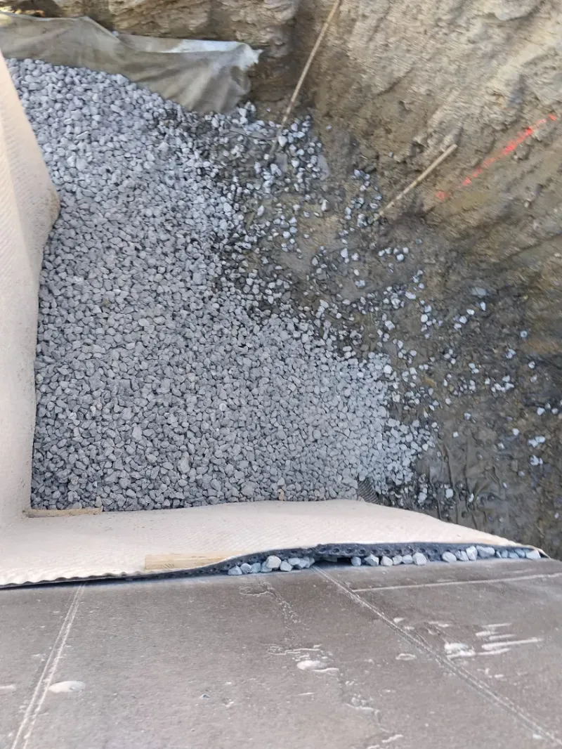 Foso de construcción relleno de grava gris junto a muros de tierra y un borde de hormigón.