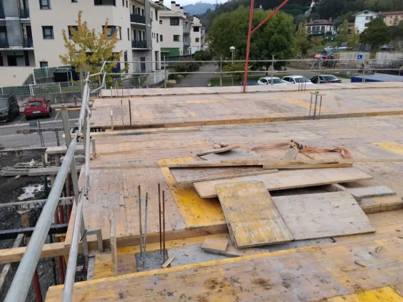 Obra en construcción en la azotea con planchas de madera contrachapada, barras de refuerzo y edificios de apartamentos vecinos al fondo.