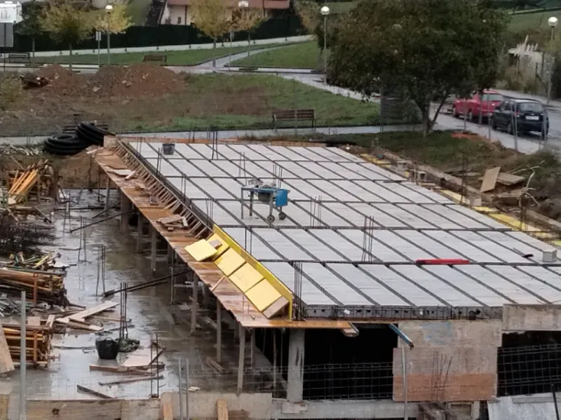 Azotea en construcción con trabajadores, estructura expuesta y materiales apilados en una obra.