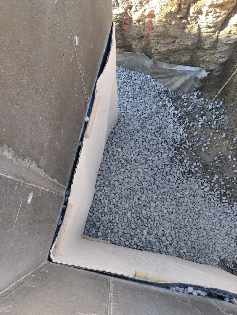 Primer plano de una cornisa de esquina con borde blanco junto a una zanja o foso exterior relleno de grava.