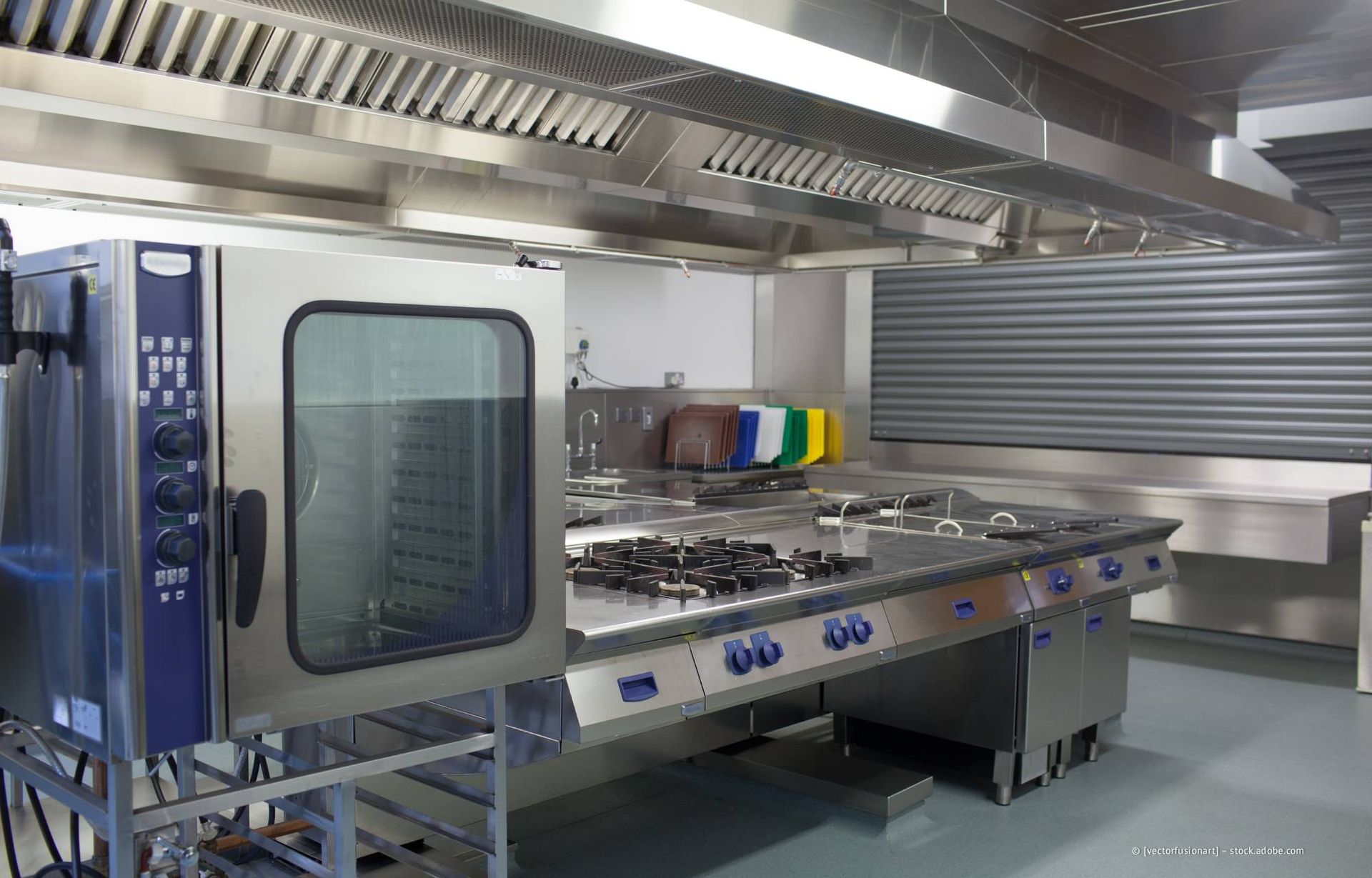 Gewerbliche Küche aus Edelstahl mit Backofen, Kochfeld und Dunstabzugshaube.