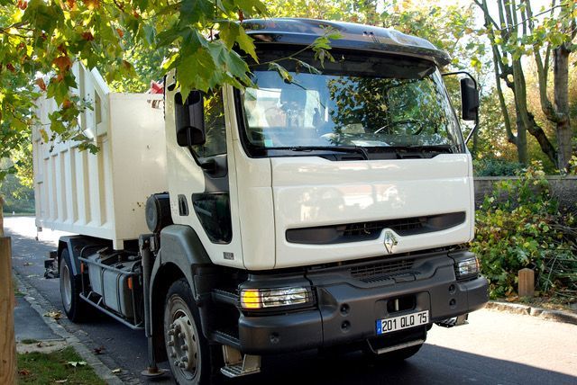 Camion cargo blanc stationné sur une route bordée d'arbres, vu de l'avant gauche.