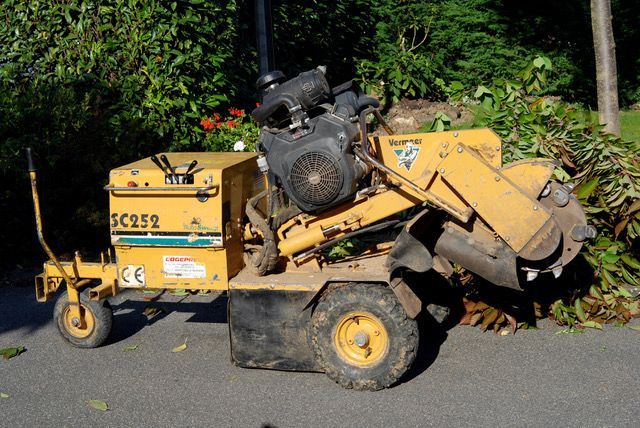 Une machine de chantier jaune, avec un moteur noir et des débris métalliques, gît sur une route bordée de verdure.