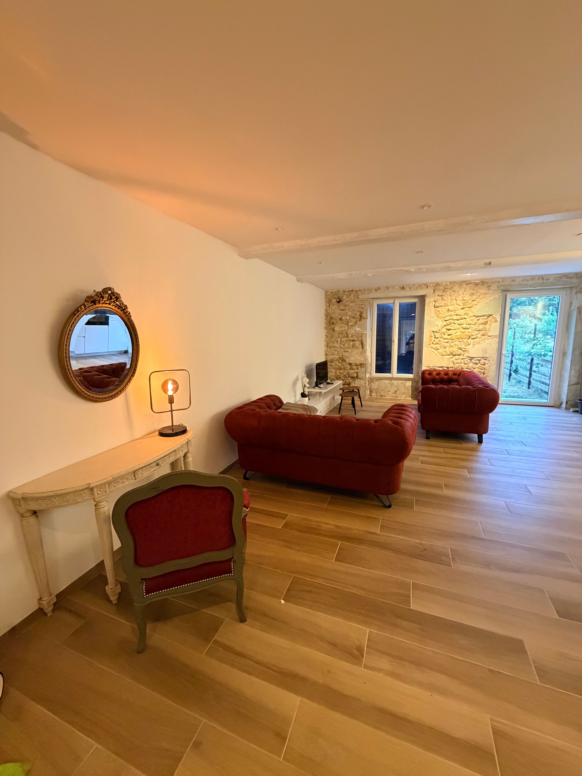 Salon avec canapés rouges et mur en pierre à Cœur de Nature Médoc