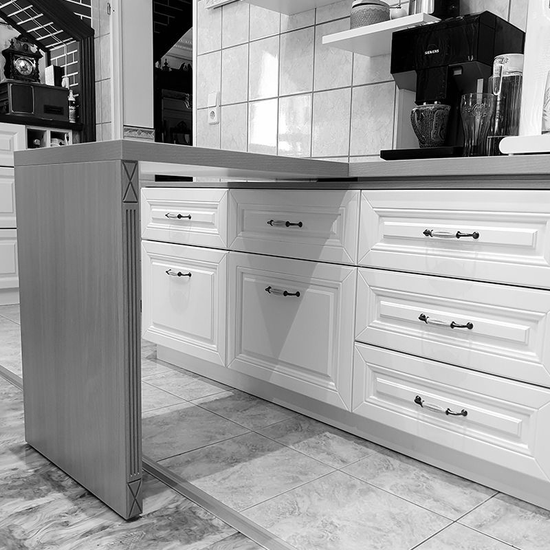 Ein Schwarzweißfoto einer Küche mit weißen Schränken und Schubladen.