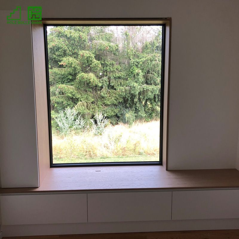 Ein Fenster mit Holzbrett und Blick auf einen Wald.