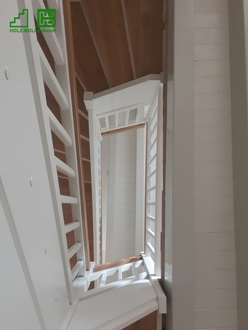 Blick nach oben auf eine Treppe mit Holzstufen und einem weißen Geländer.