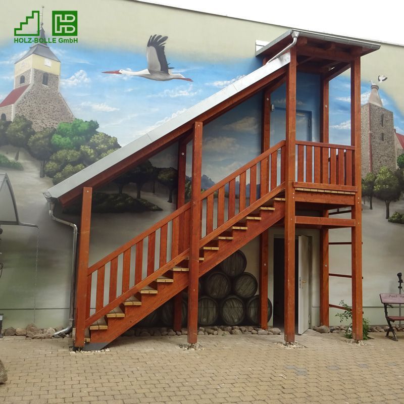 Eine Holztreppe, die zu einem Gebäude hinaufführt, an dessen Unterseite sich ein HB-Logo befindet