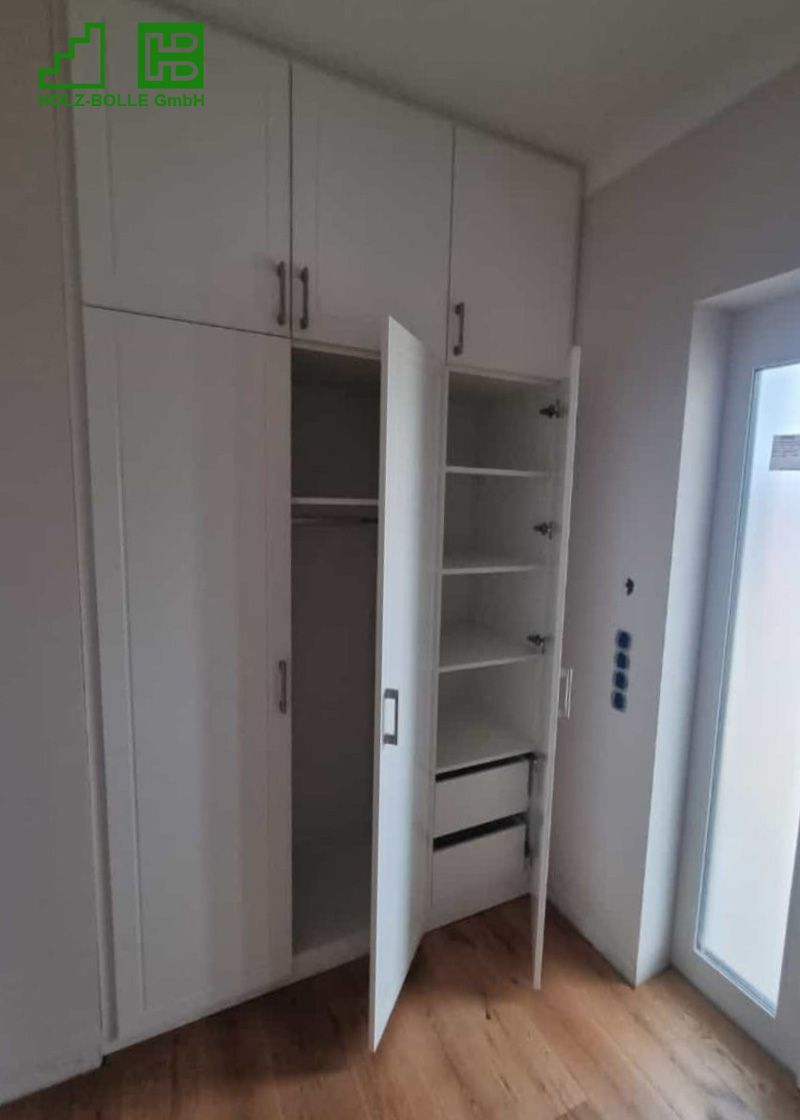 Ein weißer Kleiderschrank mit offener Tür in einem Zimmer.