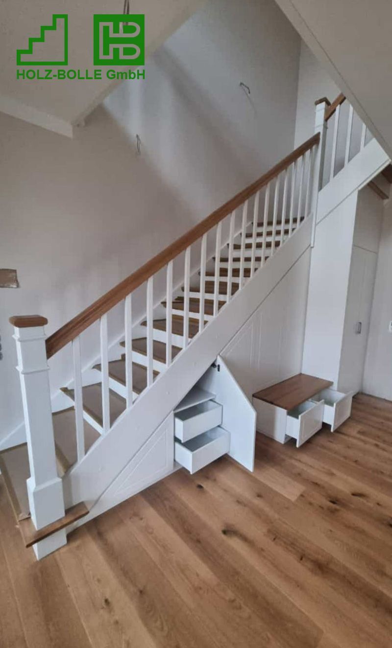 Eine weiße Treppe mit Holzhandlauf und Schubladen darunter.