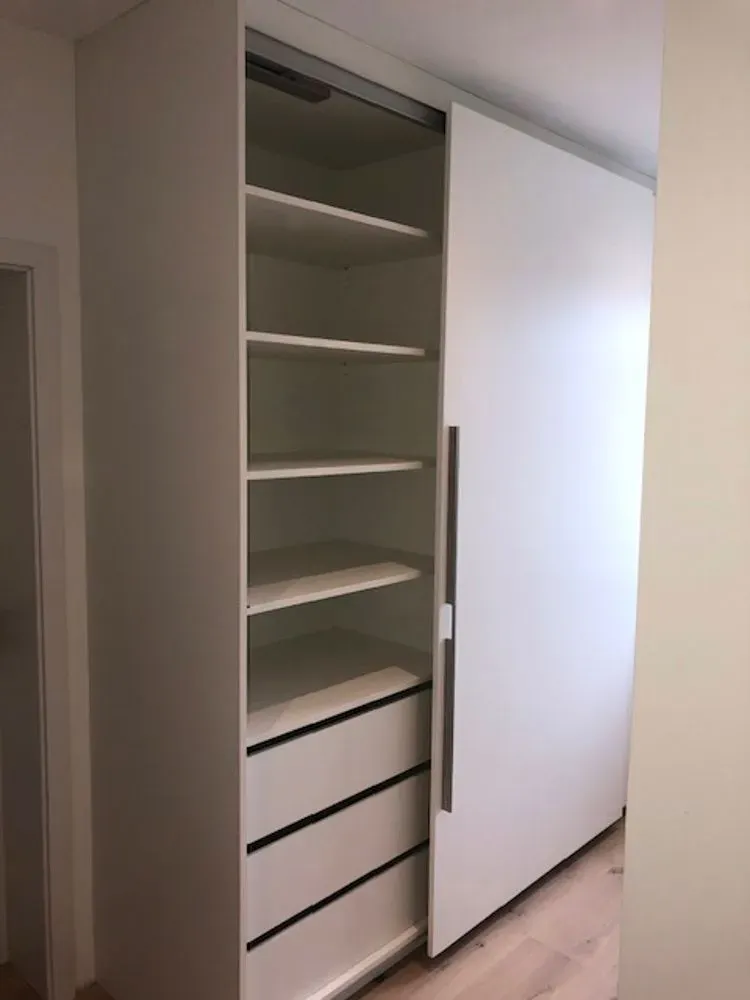 Ein weißer Schiebetürenschrank mit Regalen und Schubladen in einem Flur.