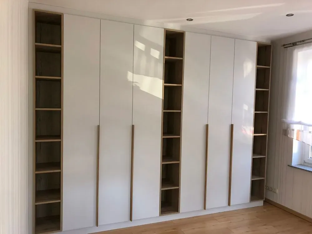 Ein großer weißer Kleiderschrank mit Holzregalen in einem Schlafzimmer.