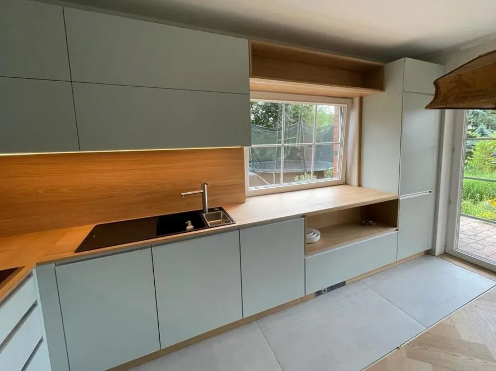 Eine Küche mit weißen Schränken, einer Spüle und einem Fenster.