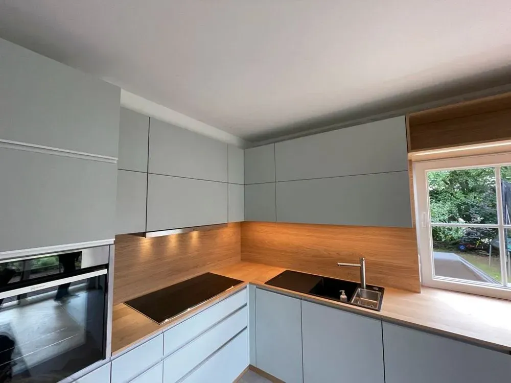 Eine Küche mit weißen Schränken, einem Herd mit Backofen, einer Spüle und einem Fenster.