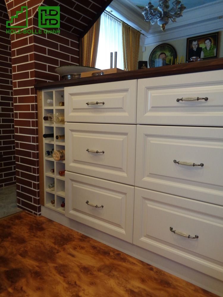 Eine Küche mit weißen Schubladen und einem Weinregal