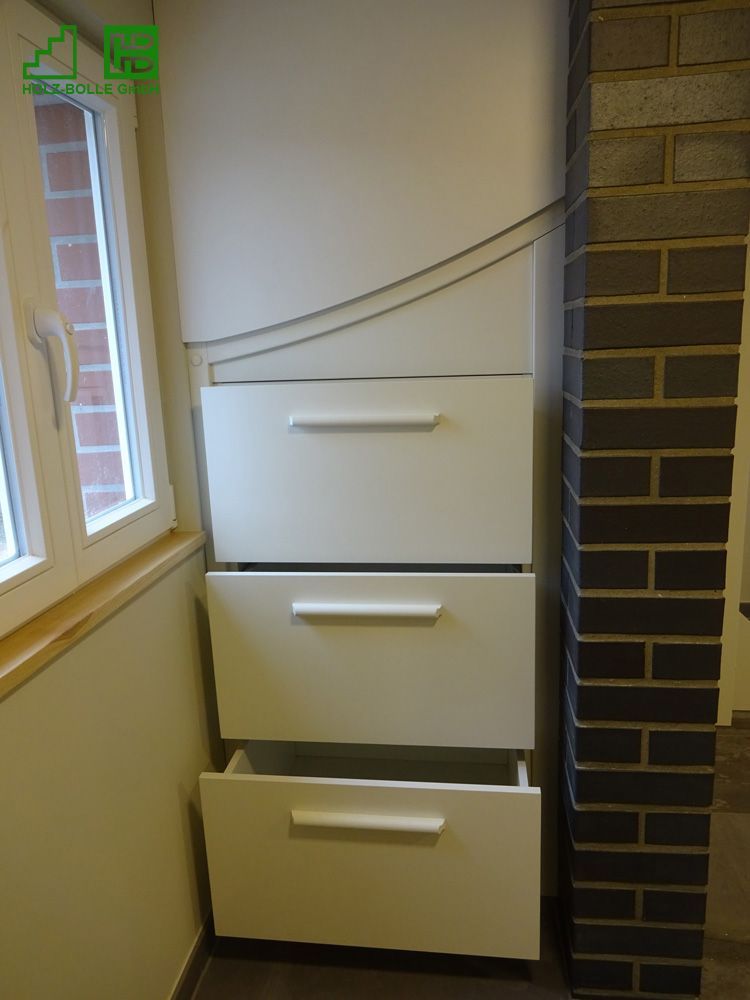 Eine Reihe weißer Schubladen unter einer Treppe neben einer Backsteinwand.