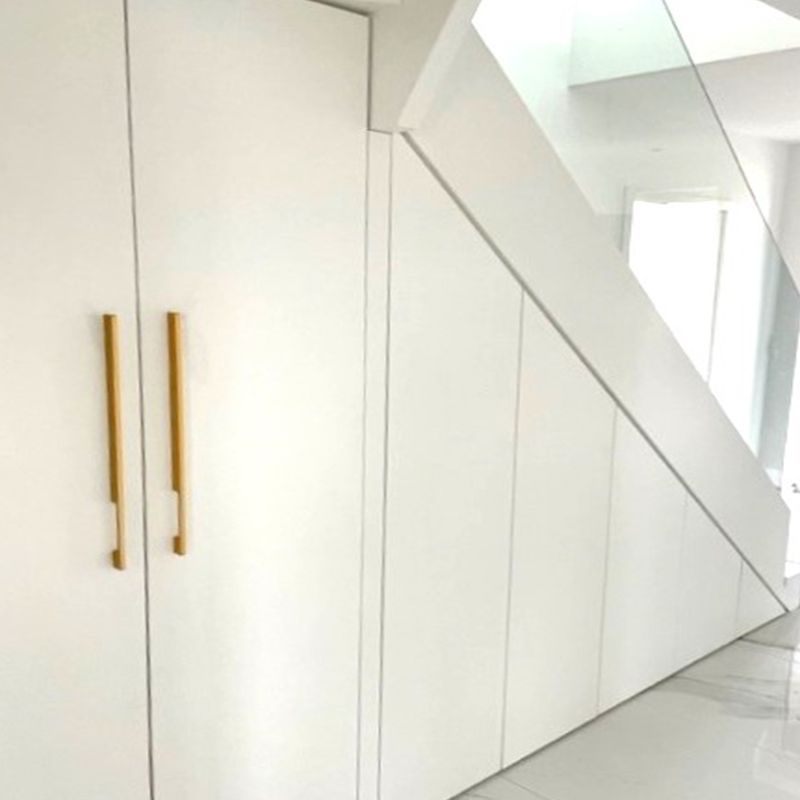 Ein weißer Schrank unter einer Treppe mit goldenen Griffen.