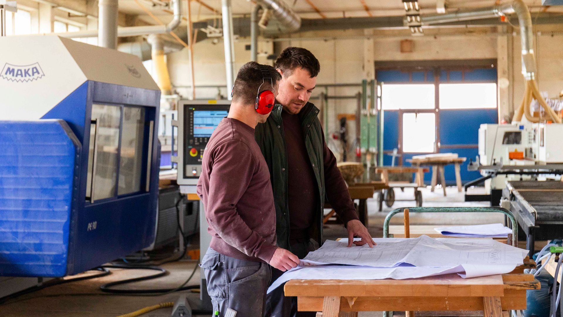 Zwei Männer stehen in einer Fabrik und schauen sich einen Bauplan an.