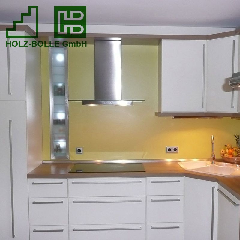 Eine Küche mit weißen Schränken und einer Dunstabzugshaube aus Edelstahl von holz-bolle gmbh