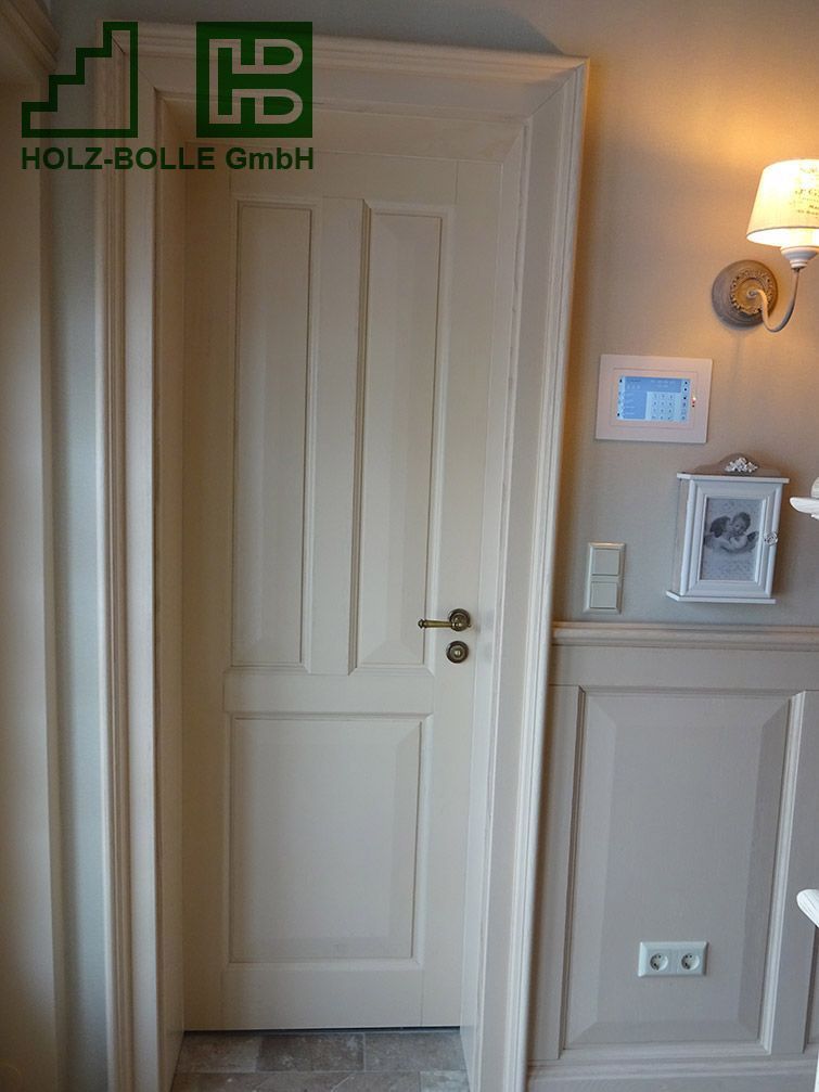 In einem Flur neben einer Wand steht eine weiße Tür.