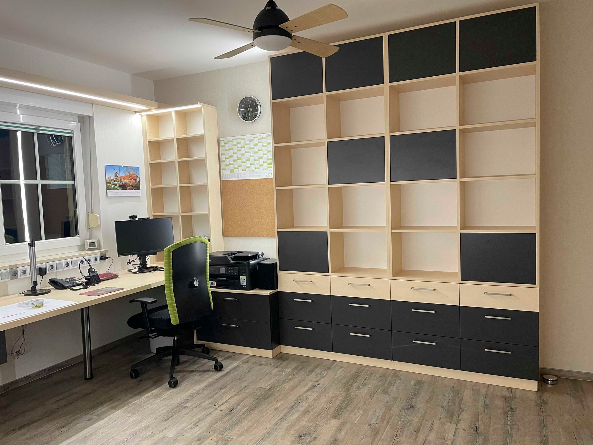 Ein Zimmer mit Schreibtisch, Stuhl, Computer und Regalen.