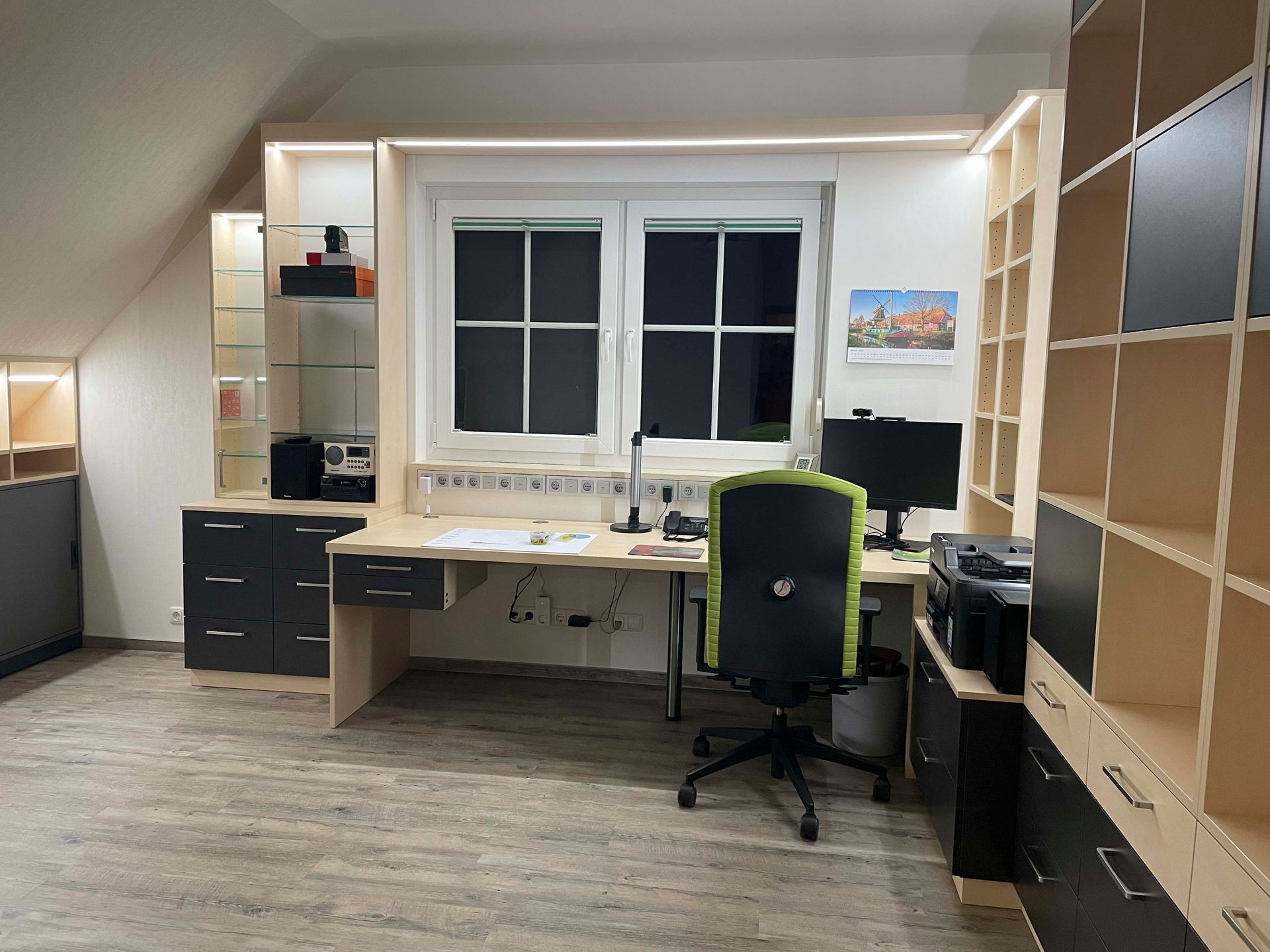 Ein Zimmer mit Schreibtisch, Stuhl, Computer und Regalen.