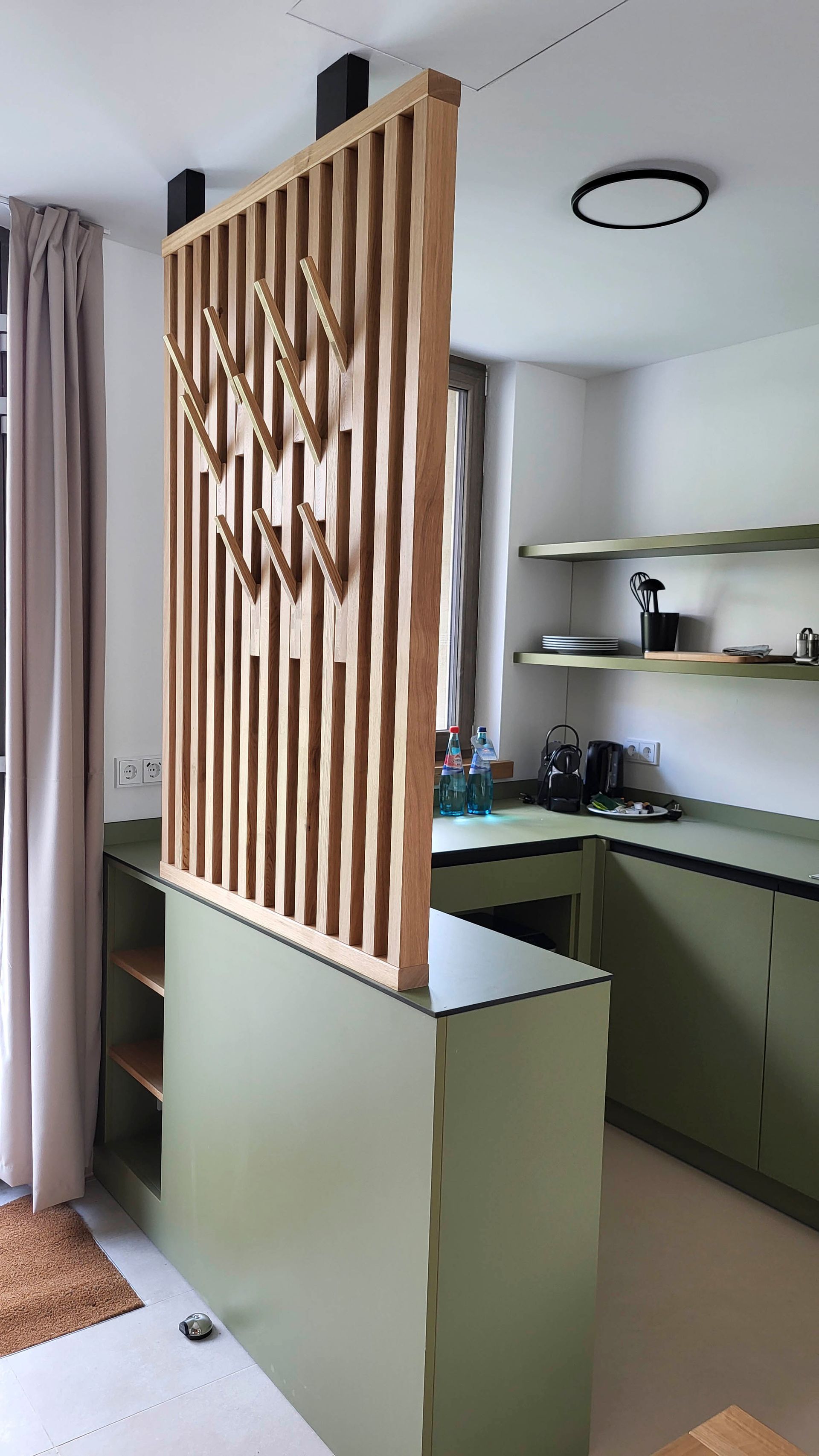 Eine Küche mit grünen Schränken und einer Holztrennwand zwischen Küche und Wohnzimmer.