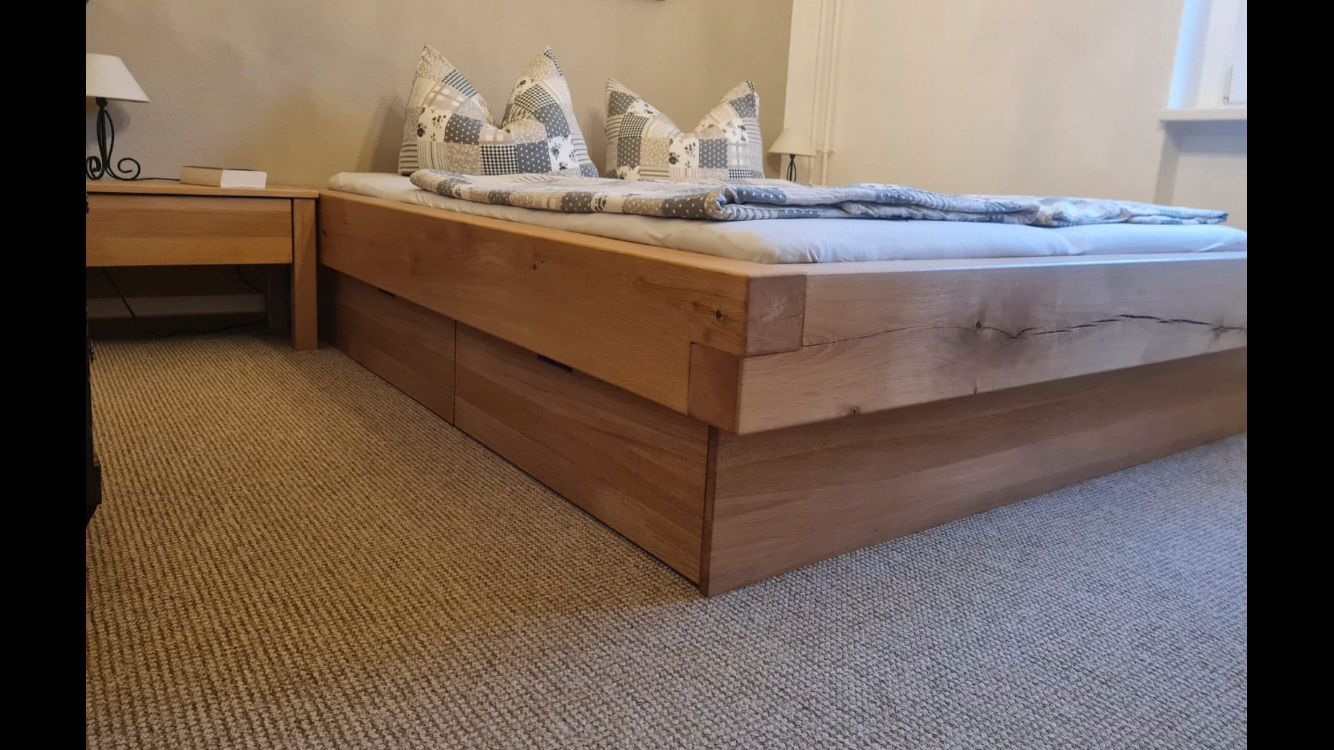 In einem Schlafzimmer steht ein hölzerner Bettrahmen auf einem Teppichboden.