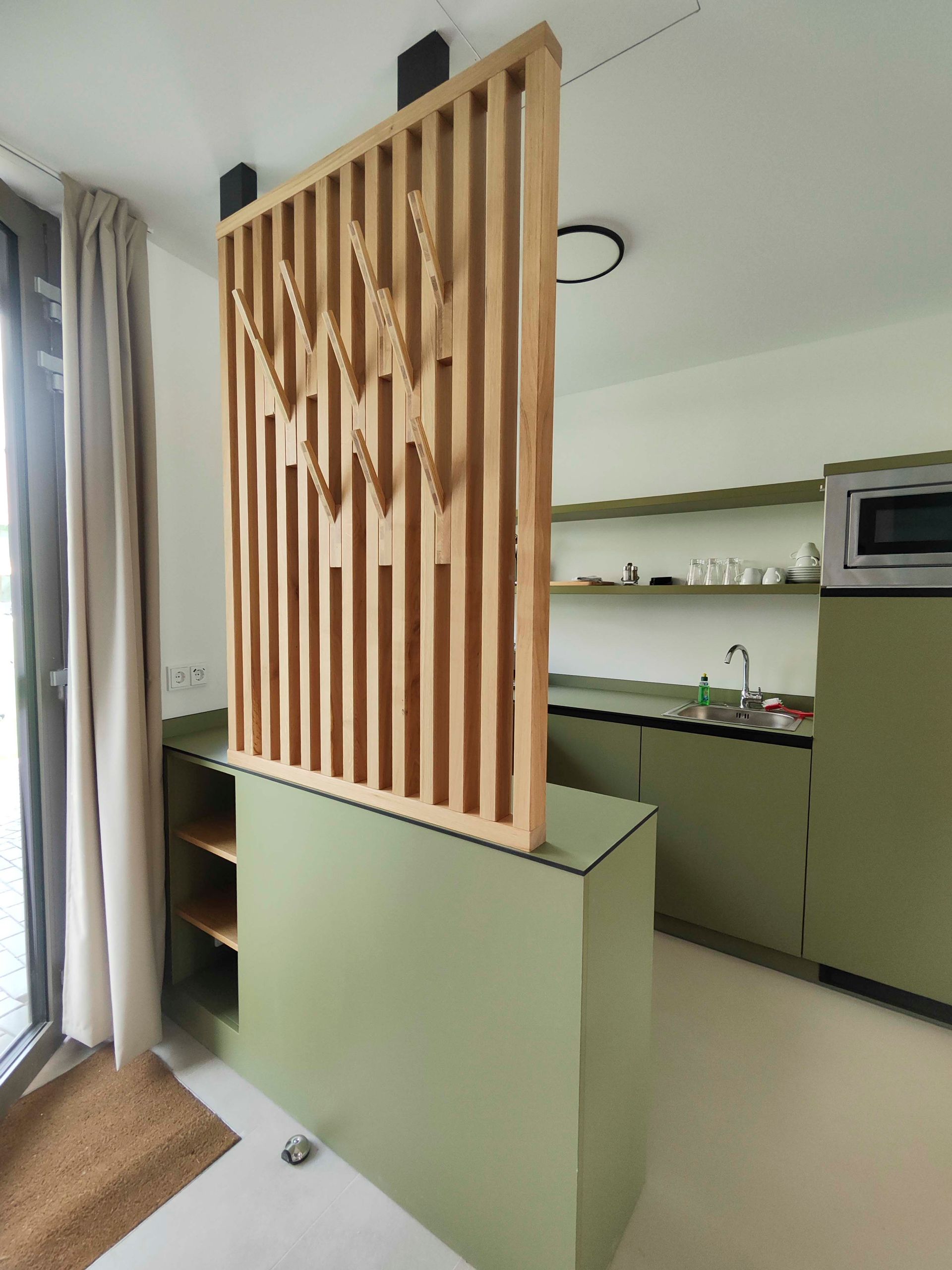 Eine Küche mit grünen Schränken und einer Trennwand aus Holz
