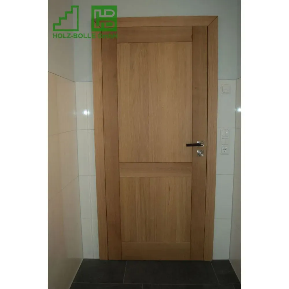 In einem Badezimmer befindet sich neben einer gefliesten Wand eine Holztür.