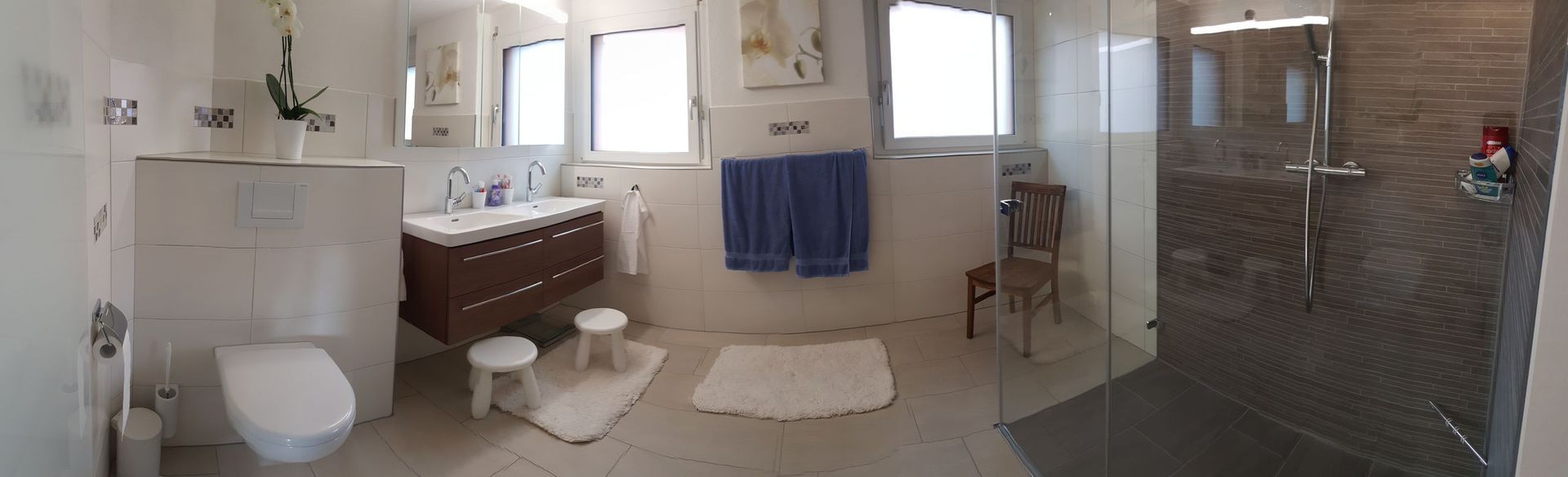Geräumiges Badezimmer mit Badewanne, Waschbecken, Toilette, blauen Handtüchern und gefliestem Duschbereich