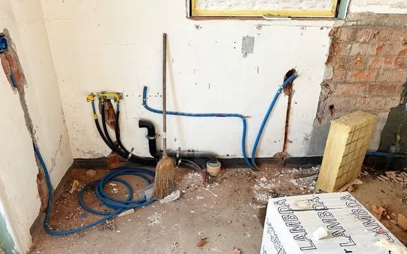 Heller, unfertiger Raum mit weissen Wänden, Fenstern, Bauschutt und Werkzeugen auf dem Boden.