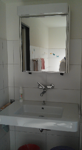 Kleines Badezimmerwaschbecken mit wandmontiertem Spiegel und verchromter Armatur.
