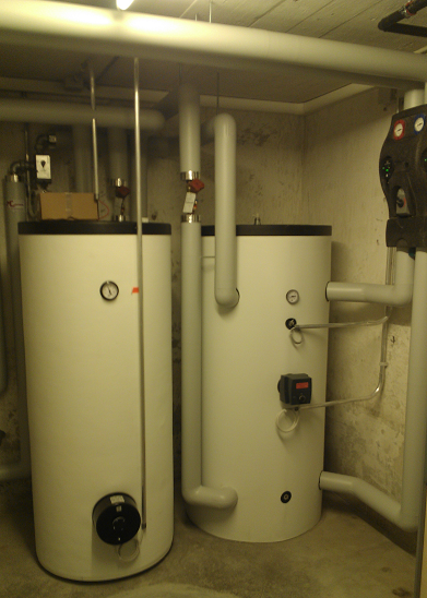 Zwei grosse weisse Warmwasserbereiter in einem Keller-Hauswirtschaftsraum mit freiliegenden Rohren und Ventilen.