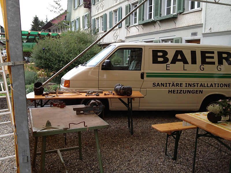 Ein beiger Lieferwagen der Firma Baier, einem Heizungs- und Sanitärunternehmen, parkte neben Tischen und Bänken im Freien.