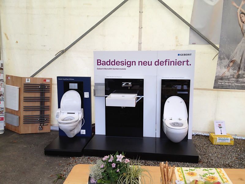 Ausstellungsstück für Badezimmerarmaturen mit zwei Toiletten, einem Waschbecken und einem deutschen Schild mit der Aufschrift „Baddesign neu definieren“.
