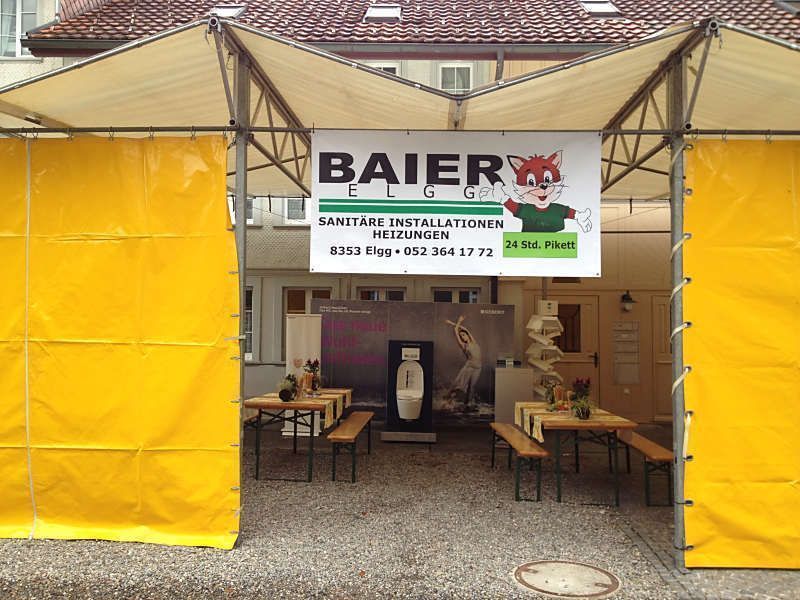 Aussenstand des Sanitärserviceunternehmens BAIER unter gelben Zeltwänden mit Tischen und einem Werbebanner